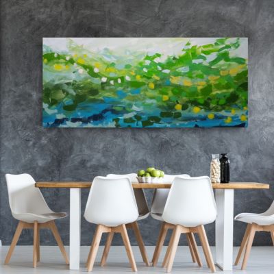 Big painting in different shades of green, blue white and yellow on a gray wall behind a wooden dining table with white chairs.