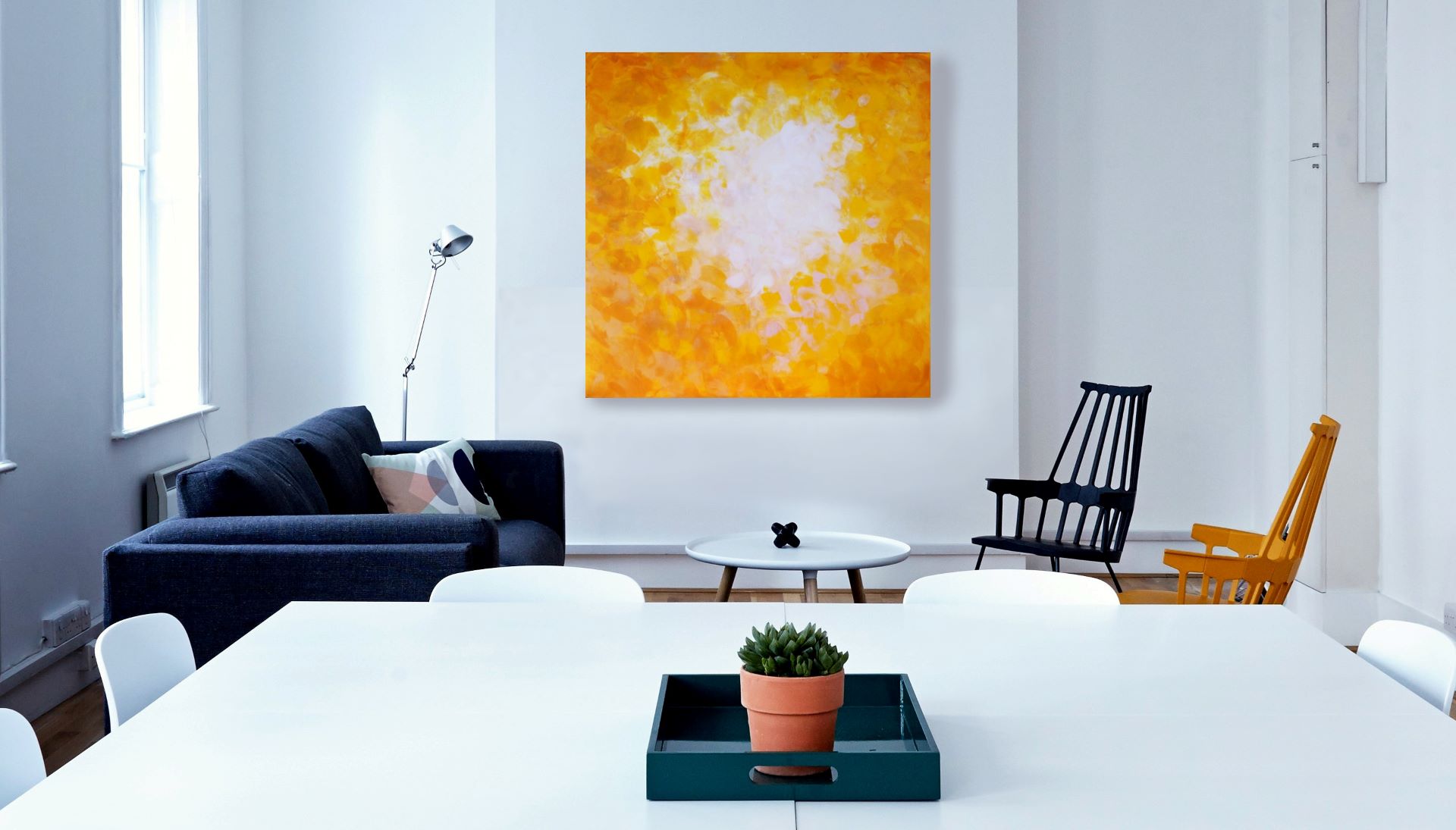 Painting in different shades of yellow and white on a white wall behind two armchairs and a table.