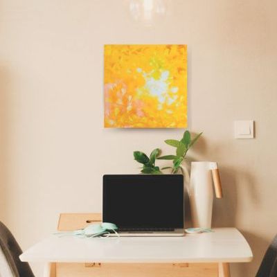 Small painting in yellow and white colors hangs on a pale pink wall on the head side of a small kitchen table with two chairs.