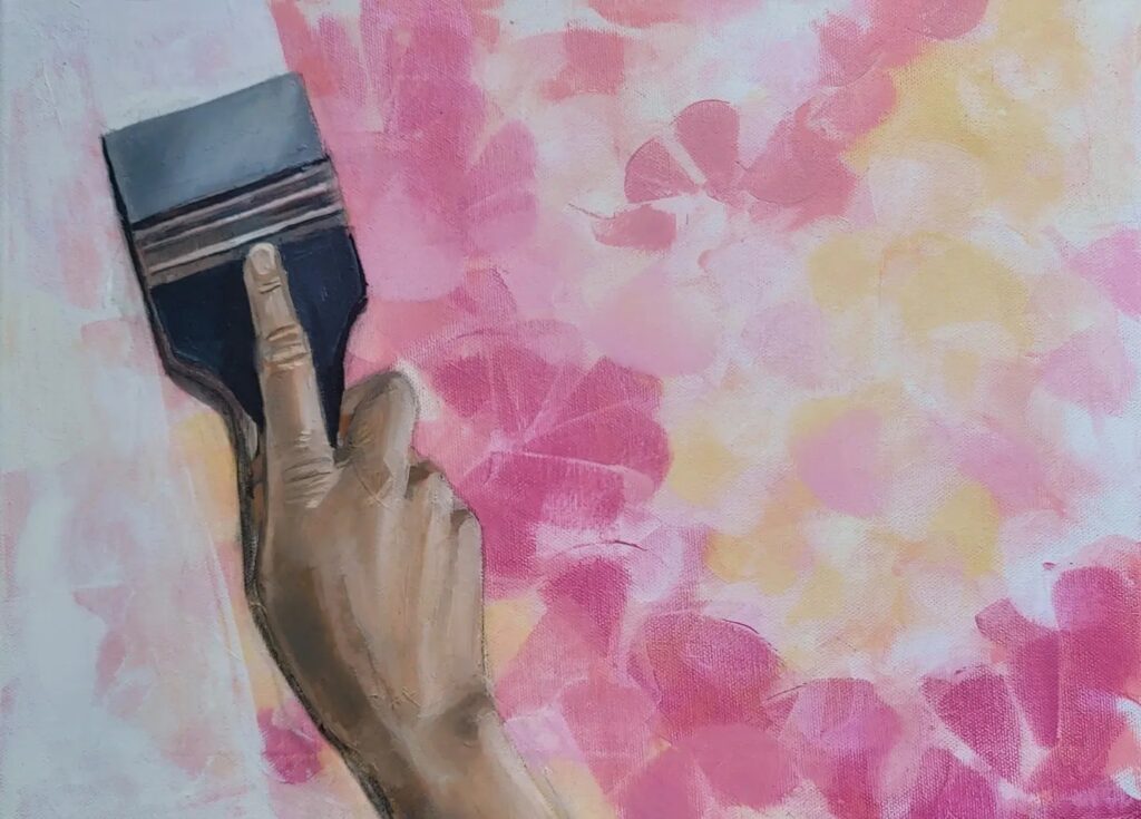 Painting in pink, yellow and white colors and a hand with a brush in front painting the left side of the canvas with white paint.