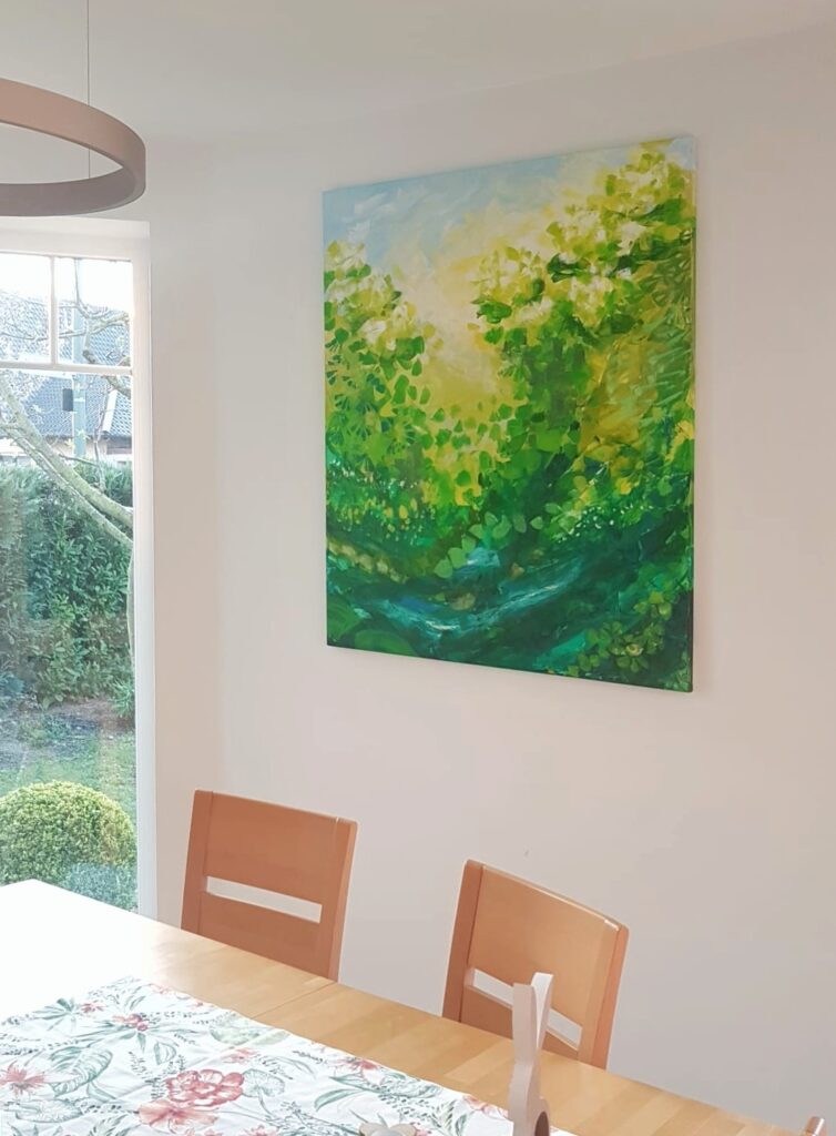 Painted picture in green, white and light blue tones hangs on the white wall behind the dining table and next to the window to the garden.