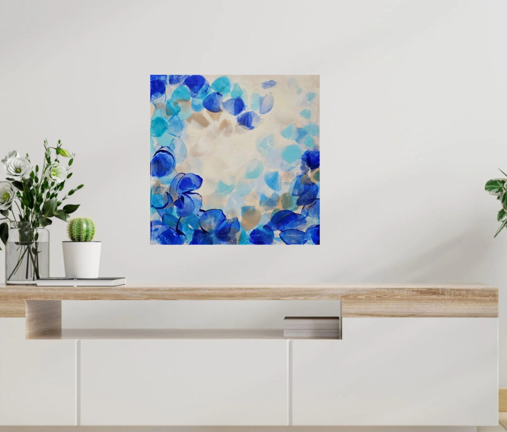 Painting in different shades of blue, beige and white colors hangs on a white wall above a wooden highboard with two potted plants.